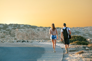 Сщгзду travel girlfriends walking along a highway, against a background of sunset and sea coast. Travel and freedom, adventures and directions for travel