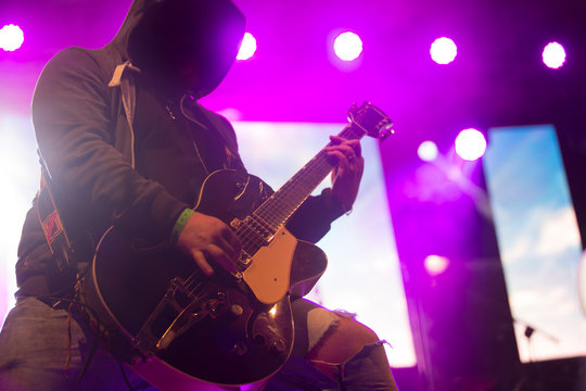 Close up scene of electric guitar player on performing stage during playing solo on concert with colourful scenic illumination via powerful lights. Unicolor simple photography
