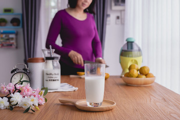 Kitchen table with Glass of milk on woman slicing fruits background.