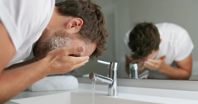 Man washing face with facial cleanser face wash soap in bathroom sink at home.