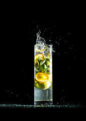 Splashes of water, lemon falling into a glass, isolated, reflection, black background. Lemonade with flying lemon and mint, isolated on a black background, free space. Cold summer lemonade.