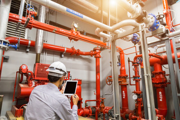 Engineer with tablet check red generator pump for water sprinkler piping and fire alarm control system.