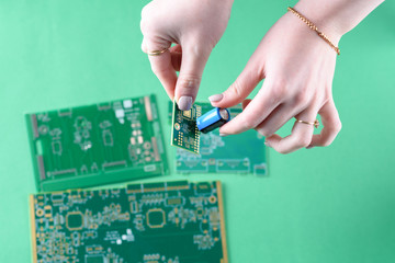 The woman technician is assembling a capacitor on the Circuit Board. The concept of computer, service, electronics, hardware, repairing, upgrade and technology. Close up of hands.