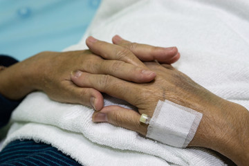 Close up old female hand of elderly patient with intravenous catheter for injection plug in hand in hospital ward room