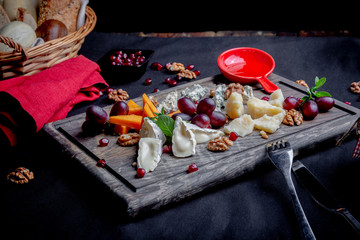 Cheese plate served with grapes, honey and nuts on a wooden background. Various types of cheese
