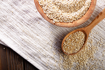 Raw organic superfood gluten free quinoa seeds in wooden spoon and bowl on kitchen table closeup