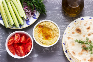 Vegan food, homemade hummus with flatbread, vegetables and olive oil on a concrete background.