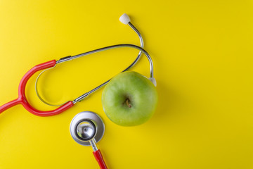 Green Apple with medical stethoscope isolated on yellow background for healthy eating. Selective focus and crop fragment. Healthy, Diet and copy space concept