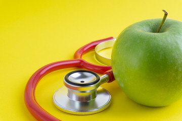 Green Apple with medical stethoscope isolated on yellow background for healthy eating. Selective focus and crop fragment. Healthy, Diet and copy space concept