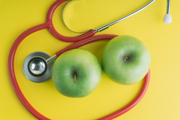 Green Apple with medical stethoscope isolated on yellow background for healthy eating. Selective...