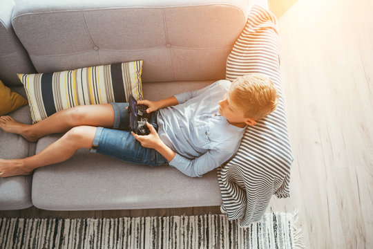 Boy laying on sofa plays with electronic devices - gamepad connected with smartphone