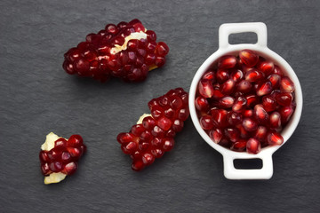 Pomegranate seeds in the white bowl on dark background. Organic fresh pomegranate in white bowl on the black stone plate.