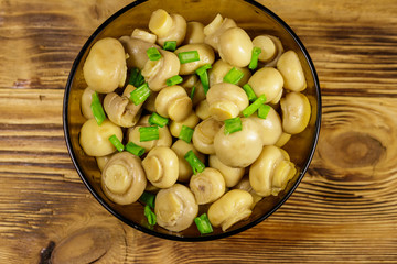 Glass bowl with pickled champignons. Marinated mushrooms on wooden table
