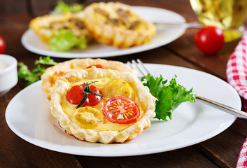 Cheddar, tomatoes tartlets on wooden background. Mini pies. Delicious appetizer, tapas, snack.
