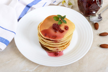 Delicious pancakes with raspberry jam on a white plate on the kitchen table. Classic American homemade breakfast.