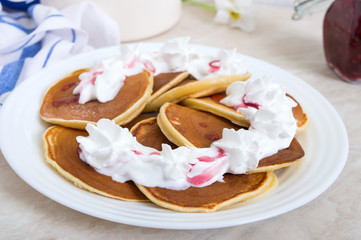Delicious pancakes with raspberry jam and whipped cream on a white plate on the kitchen table. Classic American homemade breakfast.