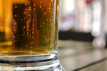 Close up of full glass of golden beer standing on wooden table in outdoor pub. Summer vacation begins. Concept of drinking problems and alcohol addiction  