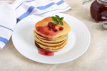 Delicious pancakes with raspberry jam on a white plate on the kitchen table. Classic American homemade breakfast.