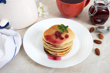 Delicious pancakes with raspberry jam on a white plate on the kitchen table. Classic American homemade breakfast.