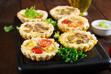 Mushrooms, cheddar, tomatoes tartlets on wooden background. Mini pies. Delicious appetizer, tapas, snack.