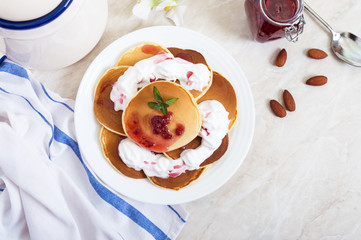 Delicious pancakes with raspberry jam and whipped cream on a white plate on the kitchen table. Classic American homemade breakfast.  The top view