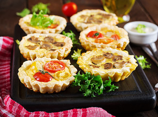 Mushrooms, cheddar, tomatoes tartlets on wooden background. Mini pies. Delicious appetizer, tapas, snack.
