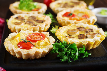 Mushrooms, cheddar, tomatoes tartlets on wooden background. Mini pies. Delicious appetizer, tapas, snack.