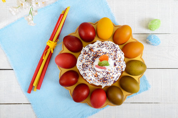 Easter cake and painted eggs on a plate on a wooden background. Easter theme. Top view.