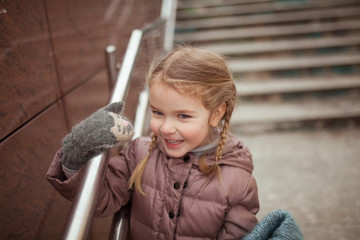 Winter walk of small pretty girl in city on background of steps