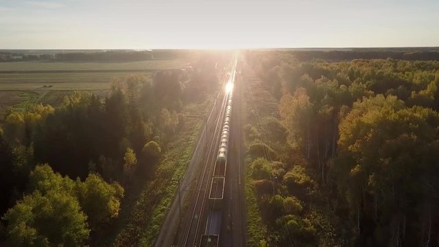 fantastic aerial view freight train drives through autumn birch forest and setting sun shines on moving cisterns 