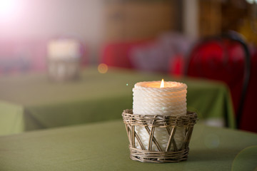 Lit up candle in wicker wooden basket standing on table in restaurant or dining room on green, natural linen tablecloth. Romantic atmosphere for couples, time for dinner. Cosy home, clean sheets