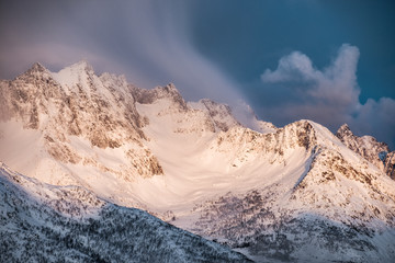 Fototapeta na wymiar Golden sunrise on snow mountain with clouds blowing on ridge