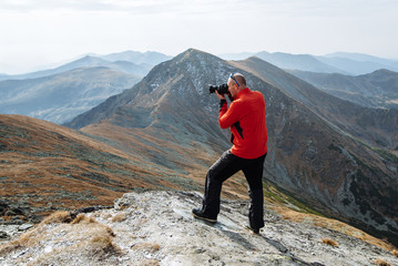 Obraz premium A young man sports athlete stands on the mountain and photographs beautiful landscapes