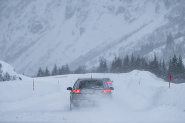 Fototapeta na wymiar Rear car driving caution through a snowstorm in the valley