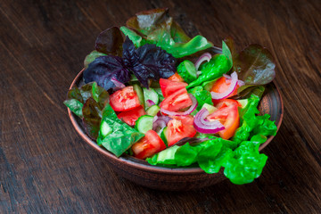 Salad with fresh vegetables, garden herbs and sun-dried tomatoes in a clay bowl on a dark wooden background