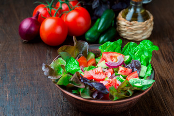 Salad with fresh vegetables, garden herbs and sun-dried tomatoes in a clay bowl on a dark wooden background