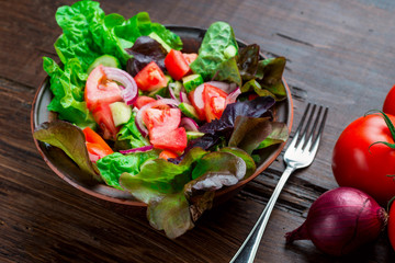 Salad with fresh vegetables, garden herbs and sun-dried tomatoes in a clay bowl on a dark wooden background