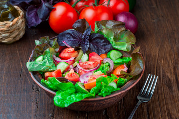 Salad with fresh vegetables, garden herbs and sun-dried tomatoes in a clay bowl on a dark wooden background