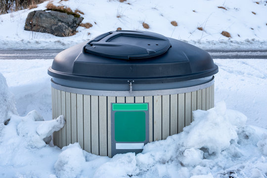 Wood trash can with black plastic covered in snow pile