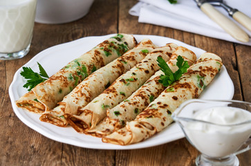 Russian pancakes with fresh green onions and parsley on a plate