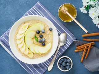 Oatmeal with bananas, blueberries, jam, honey, blue napkin on blue stone background. Close-up, top view.