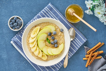 Oatmeal with bananas, blueberries, jam, honey, blue napkin on blue stone background. Close-up, top view.