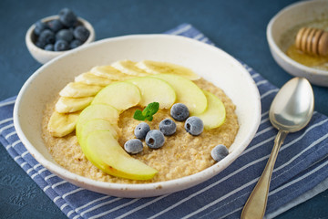 Oatmeal with bananas, blueberries, jam, honey, blue napkin on blue stone background. Close-up, side view