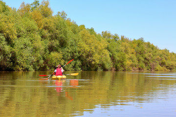 Fototapeta na wymiar Couple (man and woman) paddle a yellow kayak at Danube river. Spring kayaking and water tourism and recreational