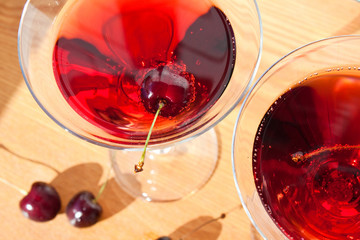 Cold alcoholic cocktail with cherry on the sunny table background