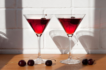 Cold alcoholic cocktail with cherry on the sunny table background