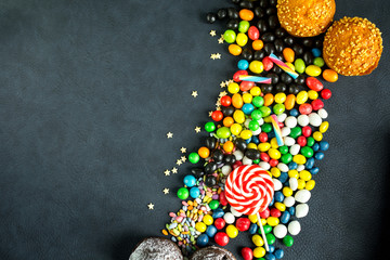 Multi-colored candies and lollipops on a dark background. Copy space and flat lay.