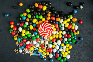 Multi-colored candies and lollipops on a dark background. Top view and flat lay.