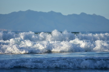 White foam of oceanic surf rolling towards camera with large landmass in distant background.