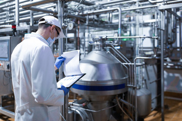 technologist taking necessary notes while standing at production department of dairy factory